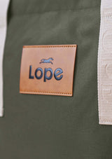 Lope Tote Bag Gröngrå stallväska rymmer mycket packning.. Tyg: 900D polyester i grågrön färg. Axelband: Vävda band i crèmevitt med nedsänkt text LOPE SPORT. Sömmar: SPI (stitches per inch): 8–9. Foder: Dubbelt tyg (samma polyester även som insida). Tråd: Nylon, med hög slitstyrka. Logo-lapp: Cognacsfärgat PU-läder med svart nedsänkt präglad logotyp. Stängningsrem: Cognacsfärgat PU-läder med tryckknapp i antik mässing präglad med logotyp