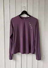 En lila långärmad tröja i ett mjukt, silkesliknande material. Tröjan har rund halsringning och ett upphöjt 3D-tryck i silikon med texten "LOPE" snett över bröstet samt "LOPE SPORT" tryckt längs ena ärmen.