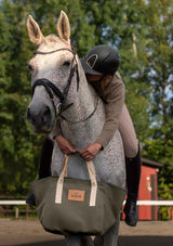 Lope Tote Bag Gröngrå stallväska. Tyg: 900D polyester i grågrön färg. Axelband: Vävda band i crèmevitt med nedsänkt text LOPE SPORT. Sömmar: SPI (stitches per inch): 8–9. Foder: Dubbelt tyg (samma polyester även som insida). Tråd: Nylon, med hög slitstyrka. Logo-lapp: Cognacsfärgat PU-läder med svart nedsänkt präglad logotyp. Stängningsrem: Cognacsfärgat PU-läder med tryckknapp i antik mässing präglad med logotyp