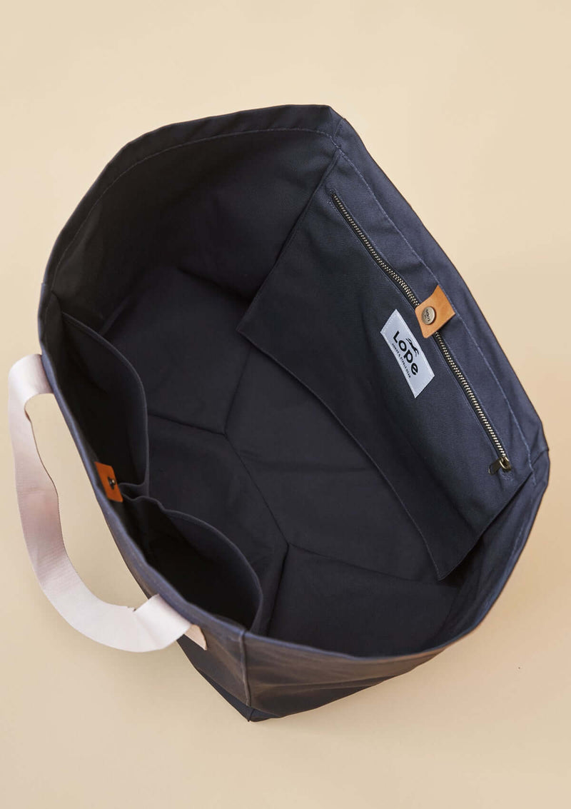 uppifrån vy av lope tote bag, stallväska Tyg:&nbsp;900D polyester i gråsvart färg. Axelband: Vävda band i crèmevitt med nedsänkt text LOPE SPORT. Foder: Dubbelt tyg (samma polyester även som insida). Logo-lapp: Cognacsfärgat PU-läder med svart nedsänkt präglad logotype. Stängningsrem: Cognacsfärgat PU-läder med&nbsp; tryckknapp i antik mässing präglad med logotype.