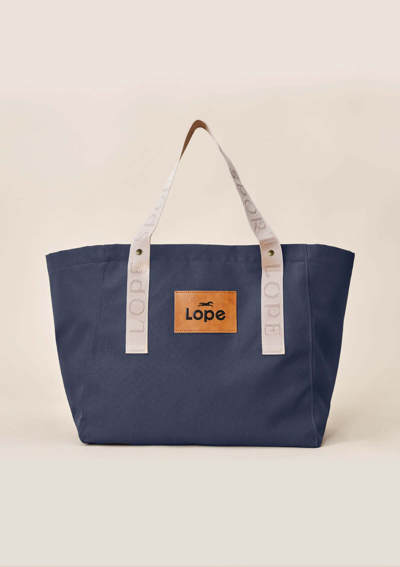 Lope Tote  midnattsblå– din nya favoritväska till stallet, jobbet och träningen. Tyg: 900D polyester i blåsvart färg. Axelband: Vävda band i crèmevitt med nedsänkt text LOPE SPORT med en nit i antik mässing Foder: Dubbelt tyg (samma polyester även som insida). Tråd: Nylon, med hög slitstyrka. Logo-lapp: Cognacsfärgat PU-läder med svart nedsänkt präglad logotyp.