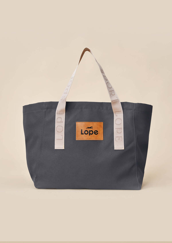 snygg lope tote bag, stallväska Tyg:&nbsp;900D polyester i gråsvart färg. Axelband: Vävda band i crèmevitt med nedsänkt text LOPE SPORT. Foder: Dubbelt tyg (samma polyester även som insida). Logo-lapp: Cognacsfärgat PU-läder med svart nedsänkt präglad logotype. Stängningsrem: Cognacsfärgat PU-läder med&nbsp; tryckknapp i antik mässing präglad med logotype.