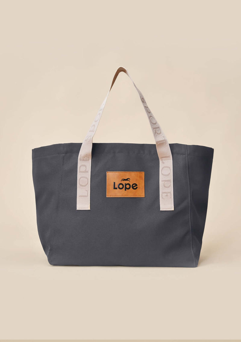 snygg lope tote bag, stallväska Tyg:&nbsp;900D polyester i gråsvart färg. Axelband: Vävda band i crèmevitt med nedsänkt text LOPE SPORT. Foder: Dubbelt tyg (samma polyester även som insida). Logo-lapp: Cognacsfärgat PU-läder med svart nedsänkt präglad logotype. Stängningsrem: Cognacsfärgat PU-läder med&nbsp; tryckknapp i antik mässing präglad med logotype.