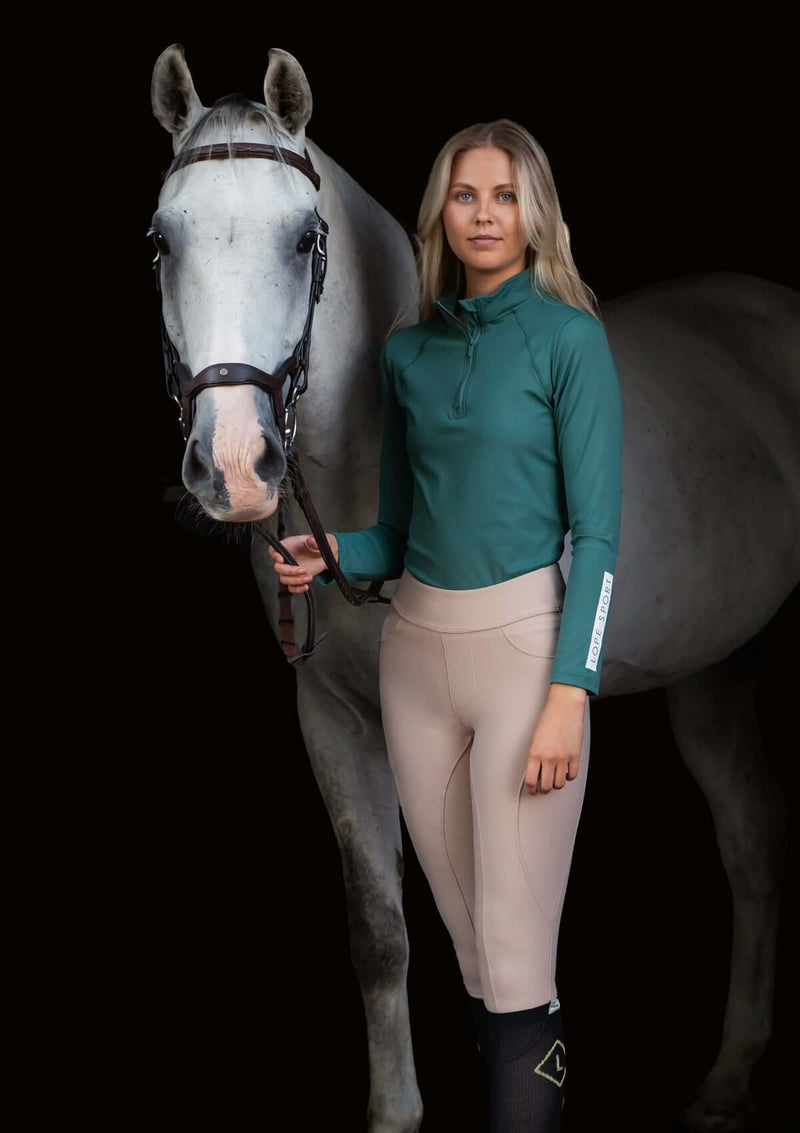 Emerald green sport topp i klassisk quarter Zip modell. Halvpolo krage med en dragkedja i matchande färg av metall. Super stretchigt funktionsmaterial som andas. Figurnära passform. Toppen har tryck på vänster ärm samt på ryggen i vitt. 