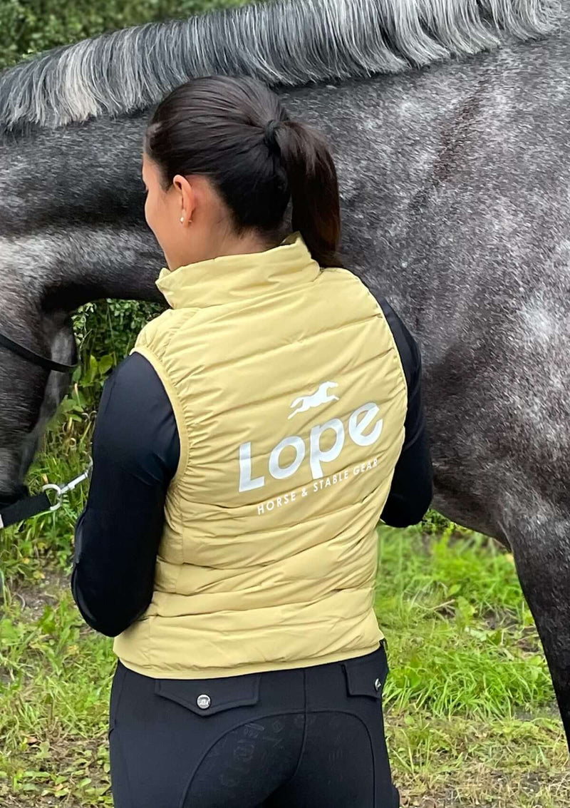 En gul dunväst för ridning med horisontella quiltade sömmar. Västen har hög krage och stort vitt tryck på ryggen med texten "Lope Horse & Stable Gear" samt en springande hästsilhuett ovanför loggan
