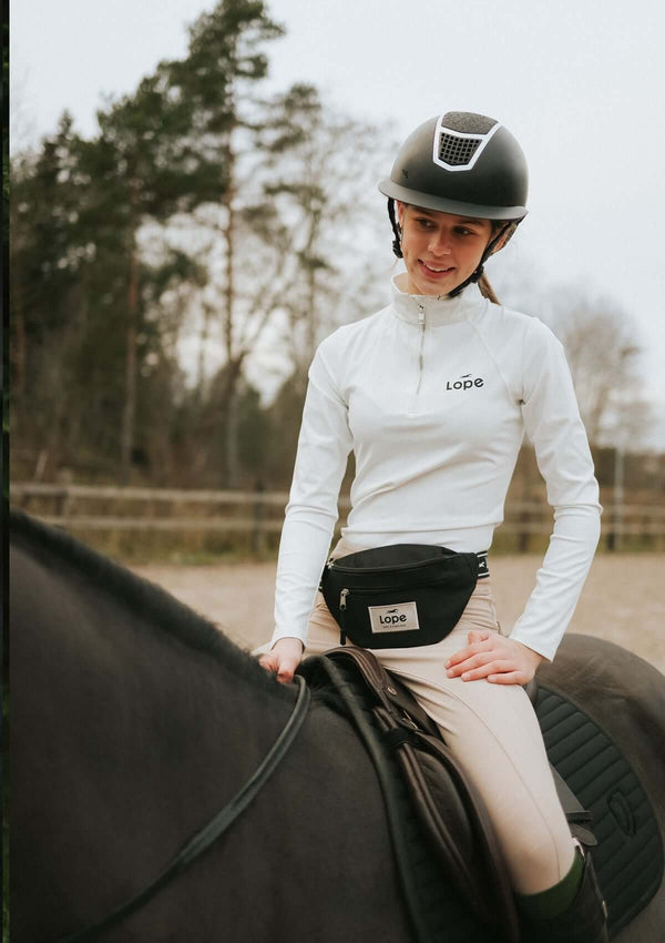 tjej till häst i vit långärmad topp i funktionsmaterial med en svart lope logotype på bröstet