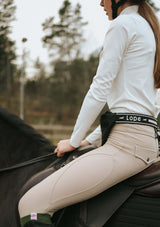 tjej till häst i vit långärmad topp i funktionsmaterial med en svart lope logo på bröstet