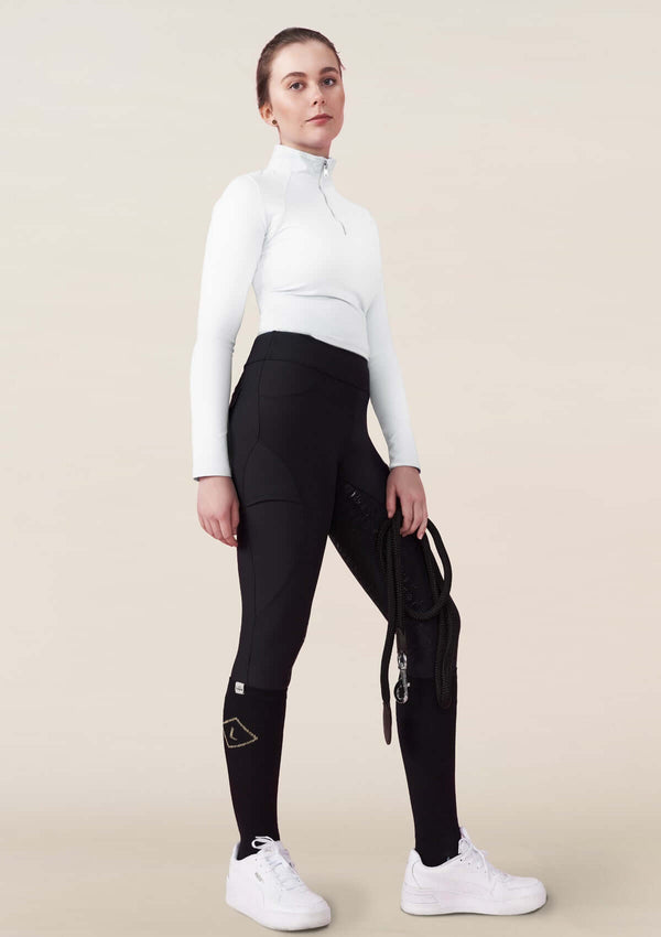 kvinna i ridkläder, svarta kompressions ridbyxor, svarta ridstrumpor med en guld romb & vit tävlings topp