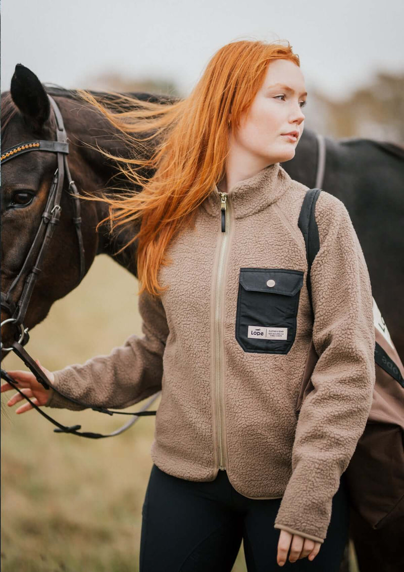  stall fleecen i mjuk teddy med ett vindtätt foder . Det tjocka, blanka blixtlåset och den svarta bröstfickan med knapp i ljus guld sätter stilen. Den feminina passformen och det något längre bakstycket ger dig både komfort och stil.