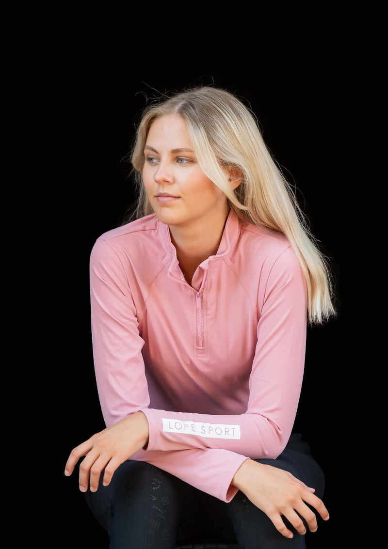 Pink blush, rosa Sport topp i klassisk quarter Zip modell. Halvpolo krage med en dragkedja i matchande färg av metall. Super stretchigt funktionsmaterial som andas. Figurnära passform. Toppen har tryck på vänster ärm samt på ryggen i vitt. Mjuk och följsa