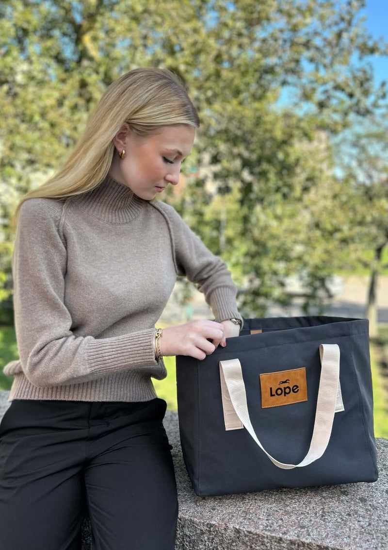 lope gråsvart tote bag. En stallväska med stor innerficka med dragkedja, två öppna sidofack och en tryckknapp som stänger väskan. Fronten ar en läder patch med präglad svart logotype samt gräddvita axelband med "lope sport" i relief