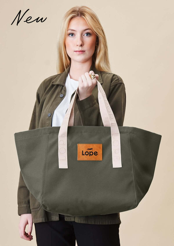 Lope Tote Bag Gröngrå stallväska. Tyg: 900D polyester i grågrön färg. Axelband: Vävda band i crèmevitt med nedsänkt text LOPE SPORT. Sömmar: SPI (stitches per inch): 8–9. Foder: Dubbelt tyg (samma polyester även som insida). Tråd: Nylon, med hög slitstyrka. Logo-lapp: Cognacsfärgat PU-läder med svart nedsänkt präglad logotyp. Stängningsrem: Cognacsfärgat PU-läder med tryckknapp i antik mässing präglad med logotyp