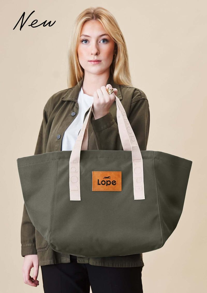 Lope Tote Bag Gröngrå stallväska. Tyg: 900D polyester i grågrön färg. Axelband: Vävda band i crèmevitt med nedsänkt text LOPE SPORT. Sömmar: SPI (stitches per inch): 8–9. Foder: Dubbelt tyg (samma polyester även som insida). Tråd: Nylon, med hög slitstyrka. Logo-lapp: Cognacsfärgat PU-läder med svart nedsänkt präglad logotyp. Stängningsrem: Cognacsfärgat PU-läder med tryckknapp i antik mässing präglad med logotyp