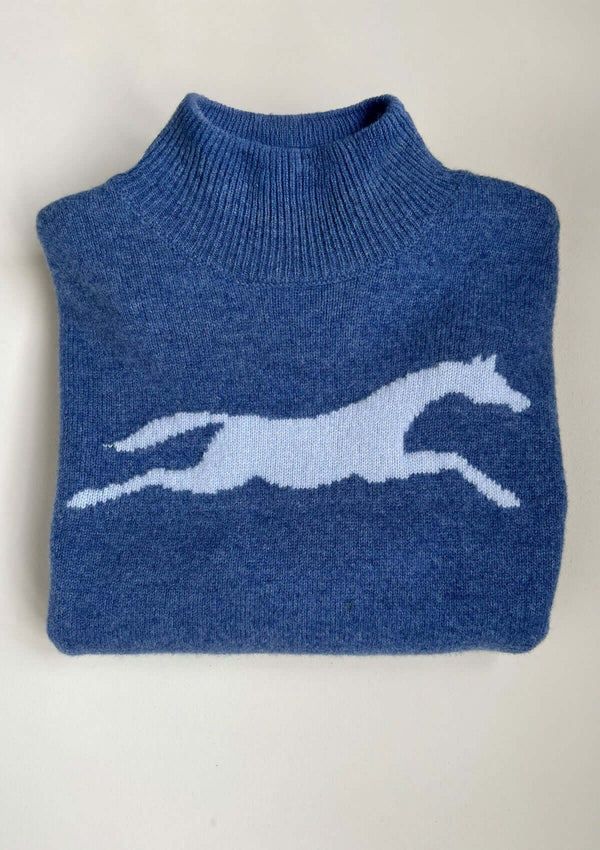 Blå långärmad, oversize finstickad tröja i 100 % ull med hästmotiv. Den har en mjukt ribbstickad halvpolo, nedhasade axlar och en avslappnad silhuett. Ribbstickade muddar vid ärmslut och nederkant samt små sprund i sidorna för en följsam passform.