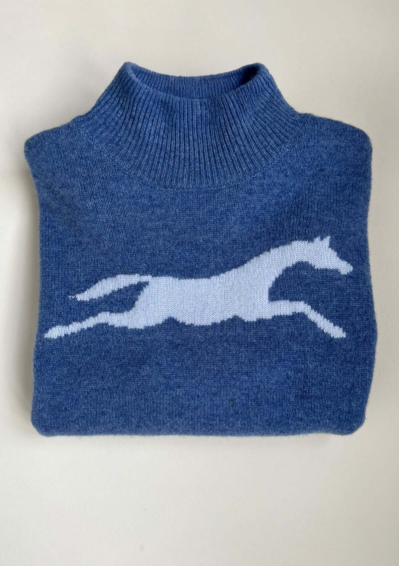 Blå långärmad, oversize finstickad tröja i 100 % ull med hästmotiv. Den har en mjukt ribbstickad halvpolo, nedhasade axlar och en avslappnad silhuett. Ribbstickade muddar vid ärmslut och nederkant samt små sprund i sidorna för en följsam passform.