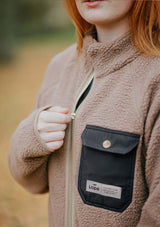 stable fleece i varm beige med svart ficka och detaljer i light gold. mjuk teddy med vindtött fodet svart framficka med lock