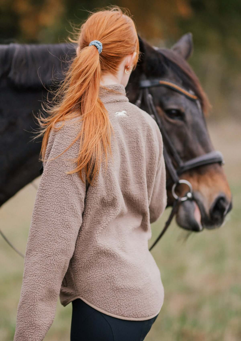 stable fleece i varm beige med svart ficka och detaljer i light gold. mjuk teddy med vindtött fodet med en broderad häst i nacken