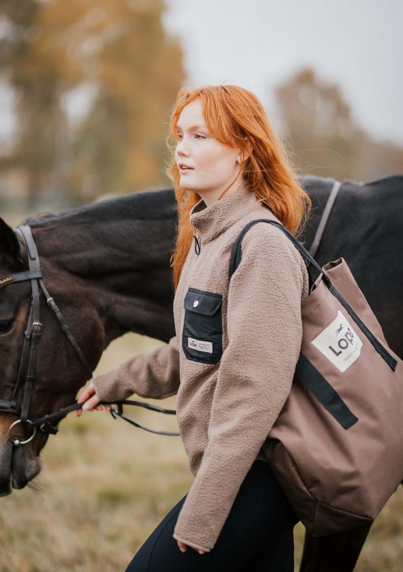 kvinlig femenin stable fleece i varm beige med svart ficka och detaljer i light gold. mjuk teddy med vindtött fodet