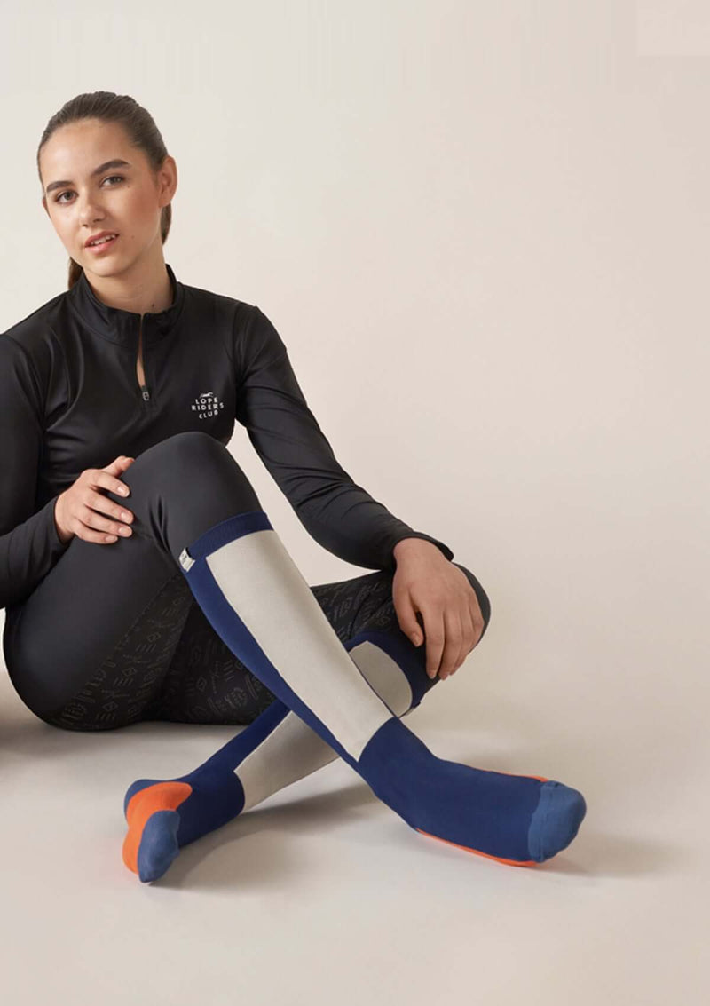 light compression riding socks, stretchy and durable blend of polyamide and elastane. blue sock with white and a orange square knee high long comfortable durable high quality performance enhancing sport socks. long sleeve riding top riding clothes quarter zip riding top four-way stretch high quality perfect fit perfect grip