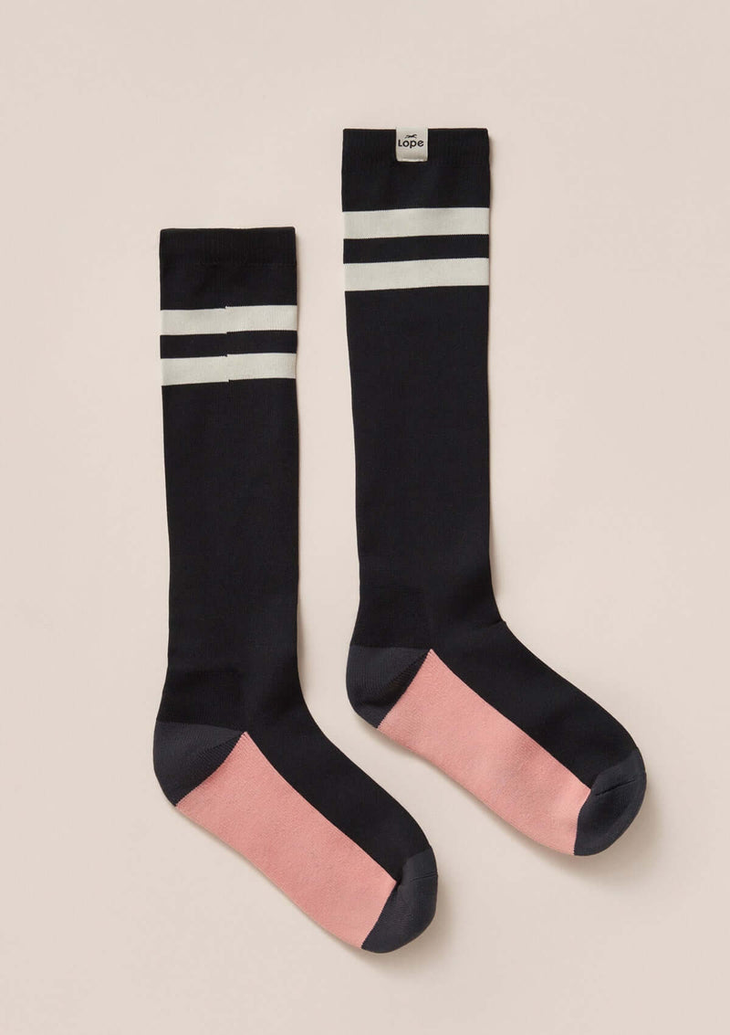 light compression riding socks, stretchy and durable blend of polyamide and elastane. black sock with white stripes and a pink square. knee high long comfortable durable high quality performance enhancing sport sockslight compression riding socks, stretchy and durable blend of polyamide and elastane. black sock with pink and off white  square knee high long comfortable durable high quality performance enhancing sport socks knähöga kompressions ridstrumpor i snygg hållbar design svarta rosa vita